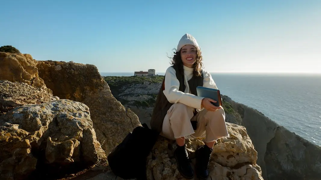 Smiling woman sitting with a book on scenic Sesimbra cliffs with ocean view.